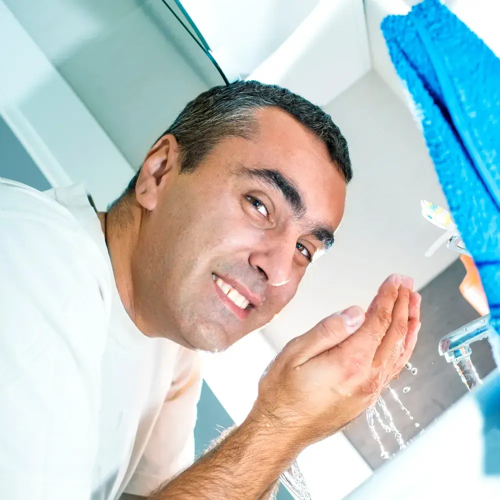 The man is washing his face at the sink