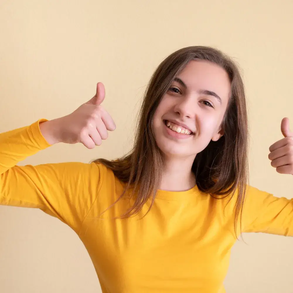 teenage girl in yellow shirt smiling and posing with two thumbs up