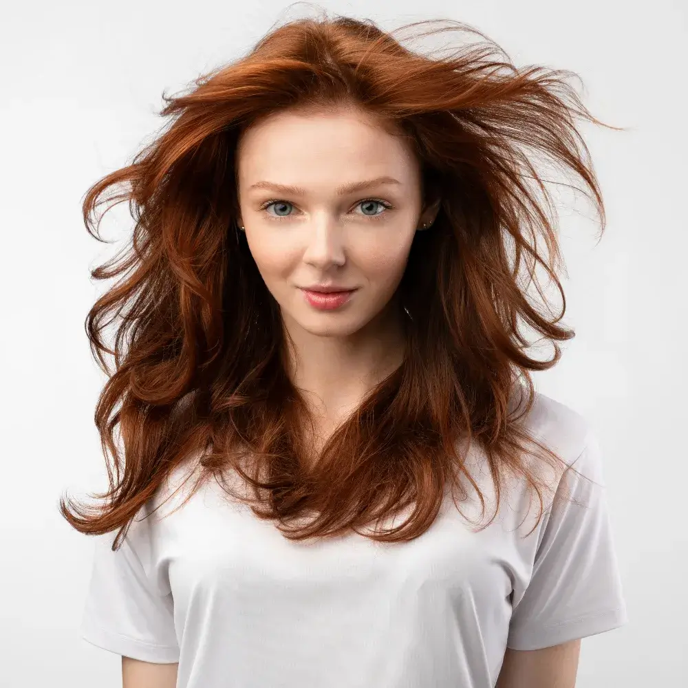 red-haired teenage girl with loose hair in white shirt posing against a white backlground
