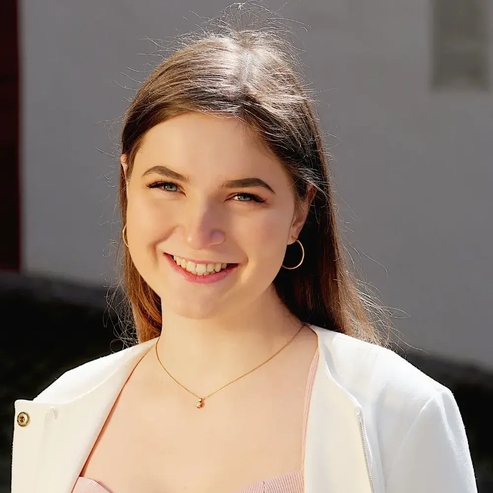 Portrait of a smiling, beautiful brunette wearing a white coat, a gold necklace, and a pair of gold hoop earrings