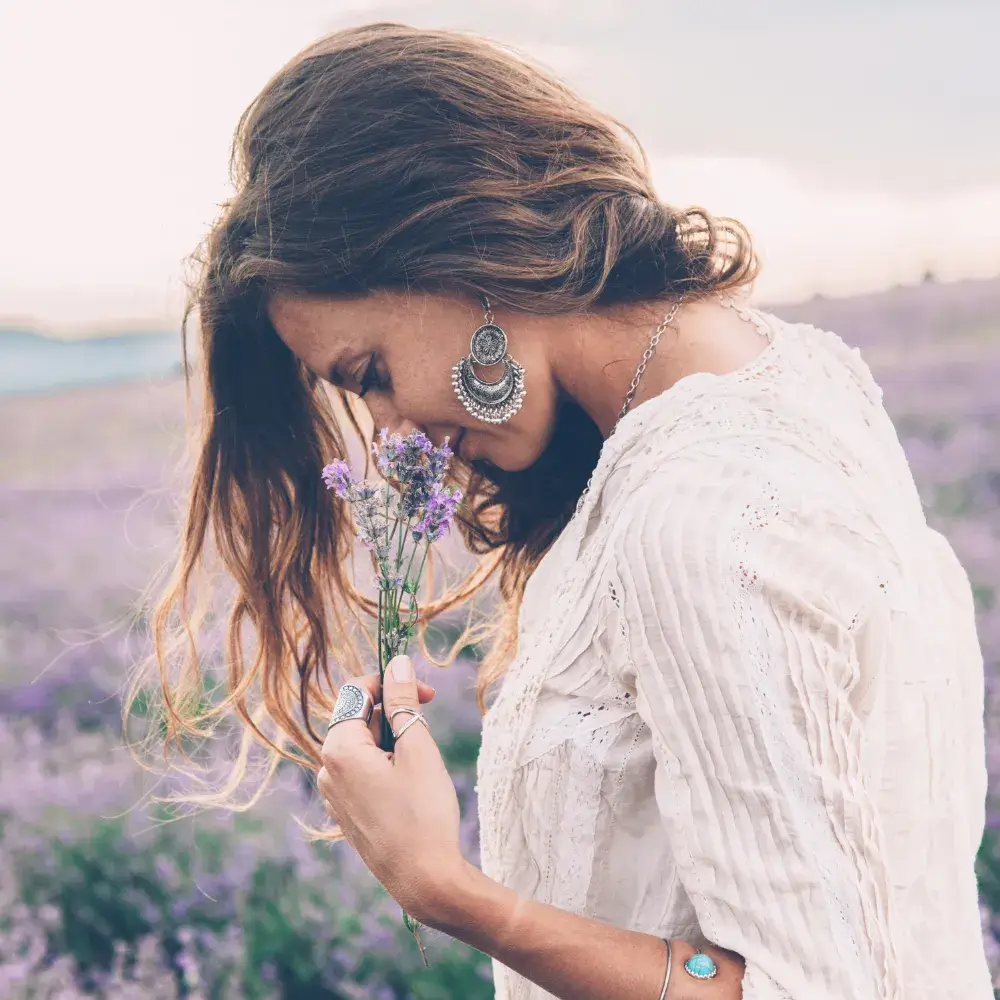 A woman wearing boho jewelry holds lavender flowers in a lavender field.