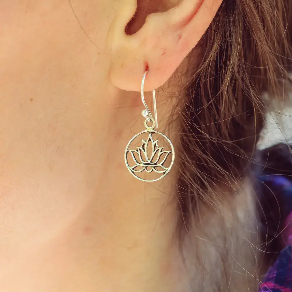 Close-up of a woman's ear adorned with a brass metal earring in a lotus flower design